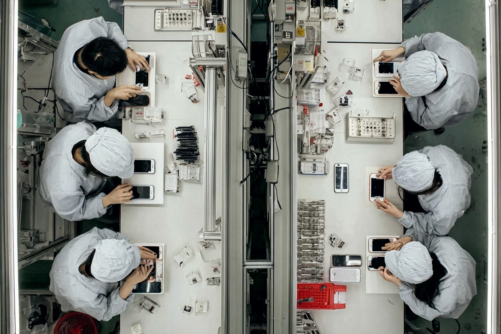 Seen from above, people assembling phones by hand along an electronics line